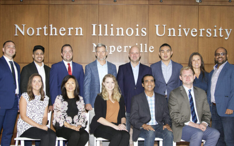 Executive MBA Class of 2023 posing in front of the Northern Illinois University Naperville sign